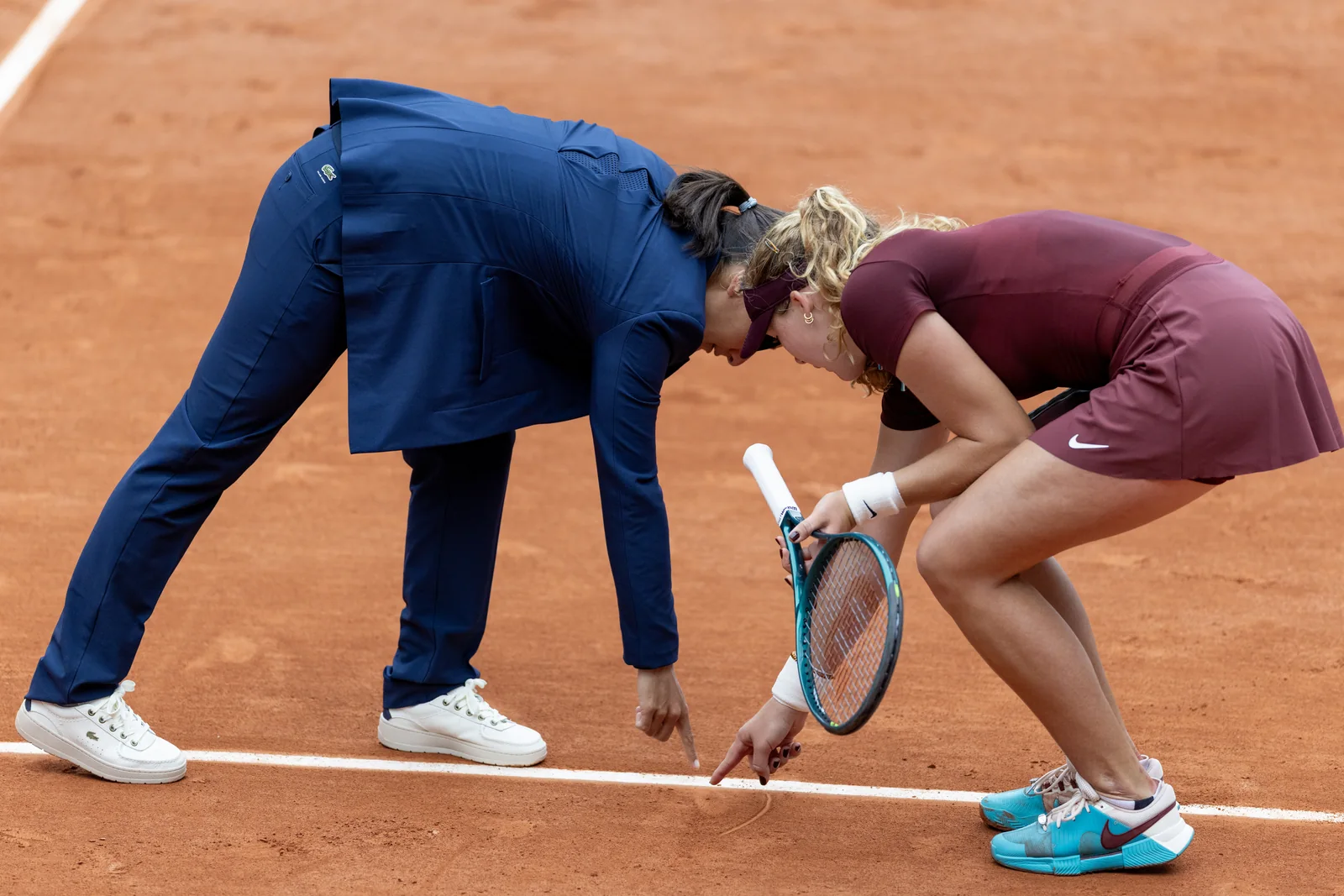 A tennis official and player looking at a ball mark on a clay court
